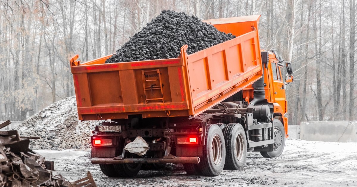 An industrial orange dump truck parked at a construction site while unloading a full load of coal.