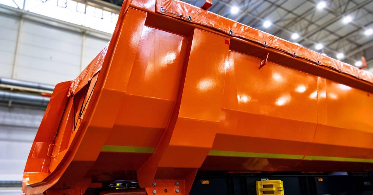 Close-up of an orange and yellow dump truck semi-axle trailer. This portion of the vehicle sits in a large storage facility.