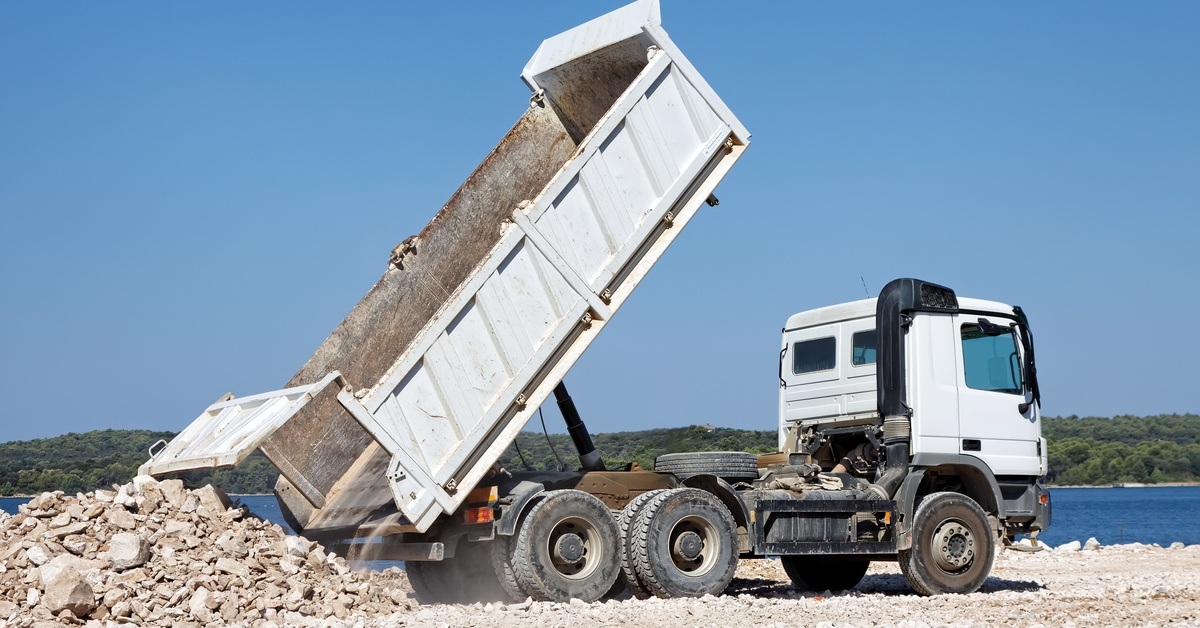 A black and white dump truck parked near a lake drops off large amounts of gravel and rocks onto a dump site.