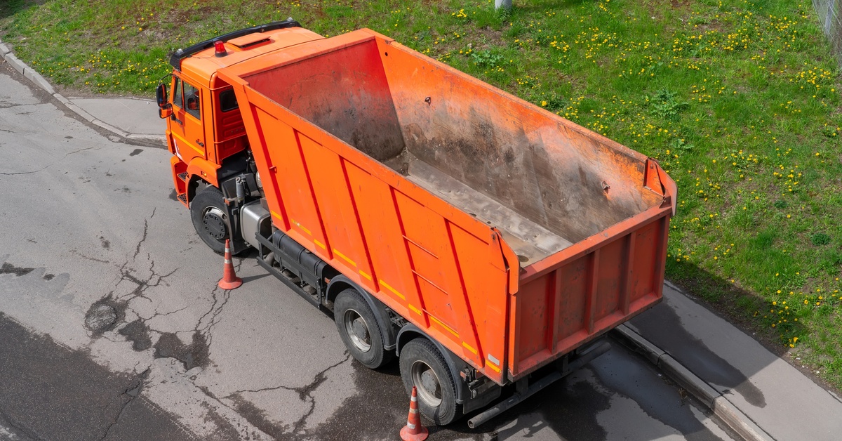 A top view of an orange dump truck parked next to some cones on the road. The truck's bed is empty.
